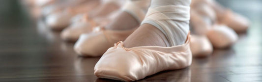 Close-up of young dancers in satin ballet shoes lined up on a studio floor, with one dancer wearing an ankle bandage—highlighting the importance of proper technique and injury awareness.