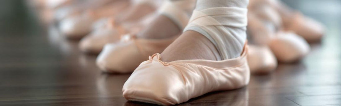 Close-up of young dancers in satin ballet shoes lined up on a studio floor, with one dancer wearing an ankle bandage—highlighting the importance of proper technique and injury awareness.