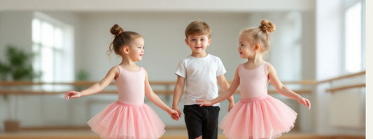 Three young children in a ballet studio, two girls wearing pink tutus and a boy in a white t-shirt and black shorts, holding hands and smiling.